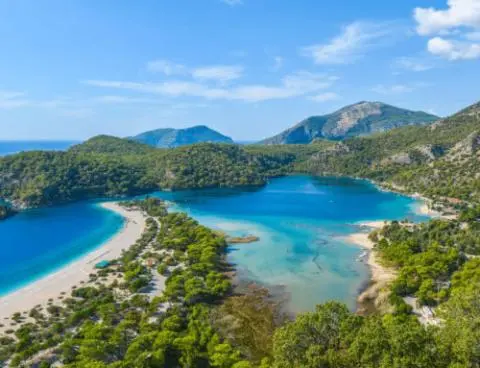 Turquoise lagoon with sandy spit and forested hills around a calm yacht harbor