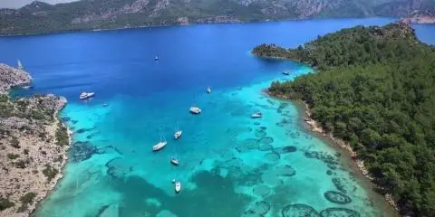Turquoise bay with sailboats anchored near rocky shoreline and clear water