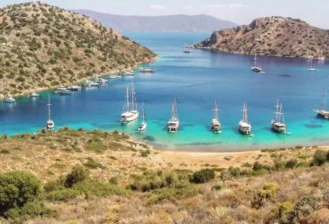 Calm turquoise bay with several small sailing gulets anchored near rocky cliffs