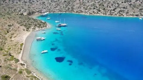 Coastal view with sail and motor yachts anchored in turquoise shallow bay near rocky shore