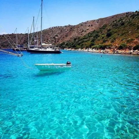 Small sailboat anchored in turquoise water near rocky coastline