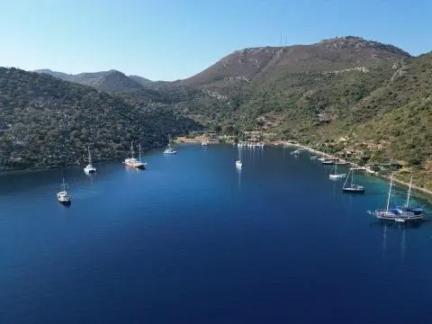 Aerial view of a bay with anchored yachts, tree-lined hills surrounding