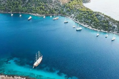Aerial view of anchored sailing yachts dotting a blue coastal cove with clear water