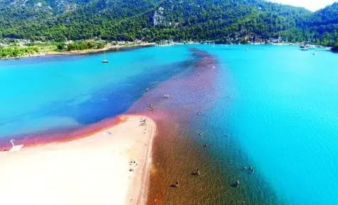 Aerial view of a sandy spit, turquoise bay, swimmers and forested shoreline in background