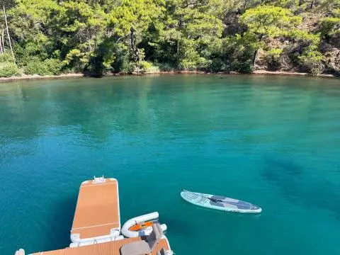 Turquoise water beside a yacht with a paddleboard on the aft platform