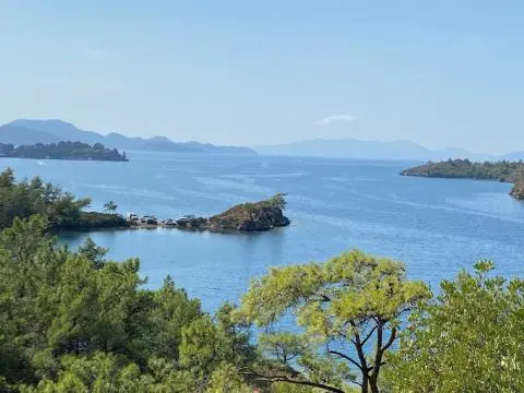 Calm coastal cove with moored boats, rocky outcrops, and green shrubbery