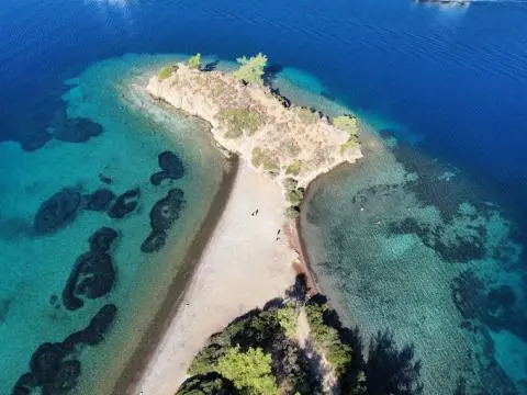 Aerial view of a narrow sandy spit with turquoise water and a yacht anchored nearby