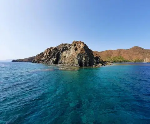 Rocky island with brown hills and clear turquoise water under a cloudless blue sky