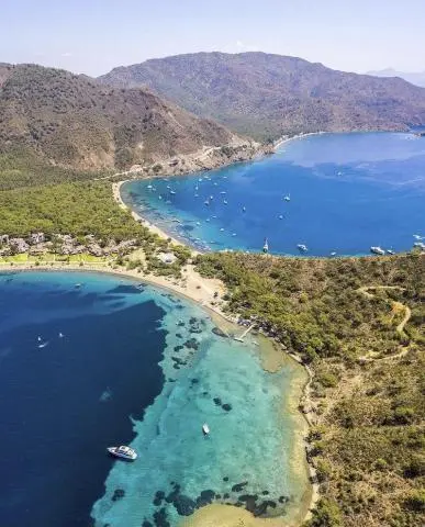 Aerial view of turquoise bay with anchored yachts along a rocky shore