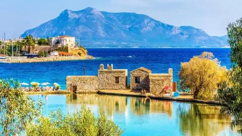 Stone boathouse on calm turquoise lagoon with distant mountain backdrop