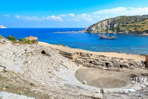 Ancient stone amphitheater ruins with a traditional sailing gulet anchored in the blue bay