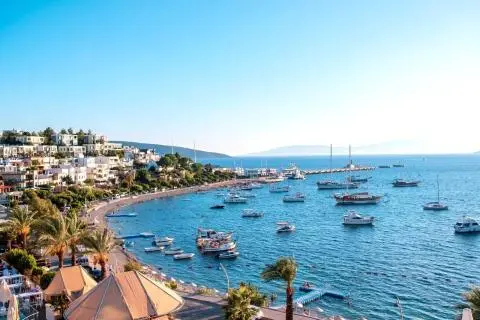 Seaside marina with sailboats and a hillside village in the background