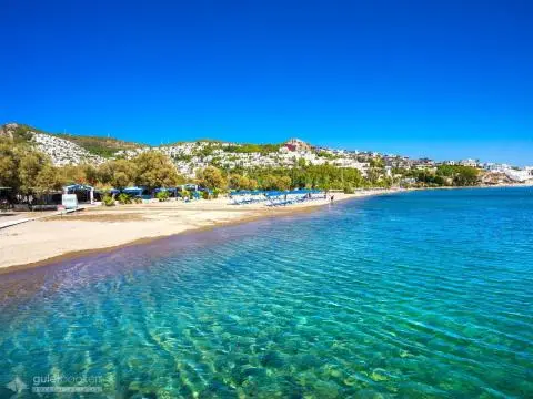 Clear turquoise sea beside sandy beach with hillside houses in the background