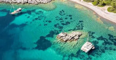Aerial view of two anchored sailboats near a rocky shoreline in turquoise water