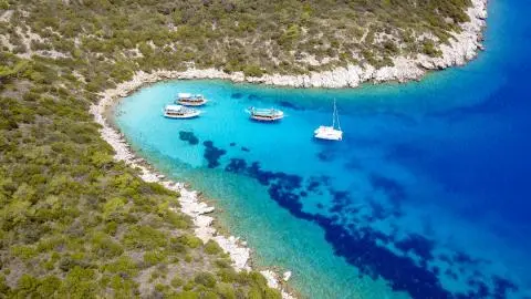 A turquoise bay with a catamaran anchored near rocky shoreline and clear blue water