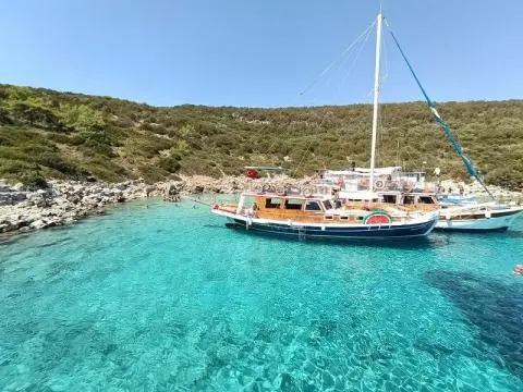 Wooden gulet anchored in turquoise bay with clear water and rocky shore