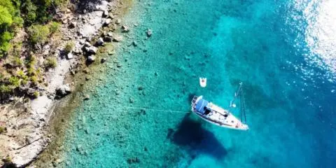 Turquoise water around a moored sailing yacht with white hull and sails
