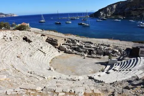 Ancient stone seating area by blue harbor with anchored yachts and clear water