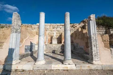 Ancient stone ruins with three marble columns and a small marble statue in the background