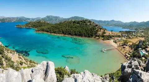 Aerial view from rocks of turquoise bay, small beach, docked boats and forested headland