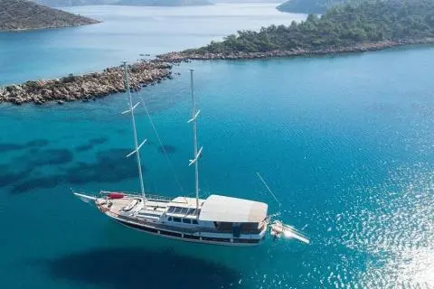 Two-masted gulet anchored in turquoise bay with clear water and coastline