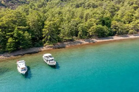 Two motor yachts anchored in turquoise water near a forested coastline