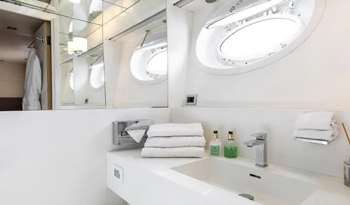 Interior yacht bathroom with white surfaces, oval mirrors, and sink area