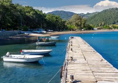 Small white motorboats tied to a wooden pier with forested shoreline and hills