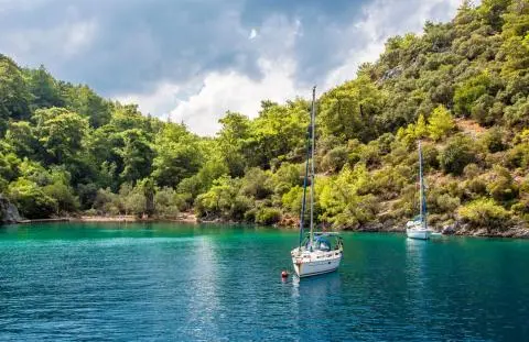 Two sailboats anchored in turquoise cove with forested hills backdrop