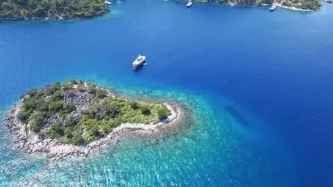 White yacht anchored beside a small rocky islet with trees in deep blue sea