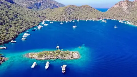 Turquoise bay with small island and several anchored boats in clear blue water