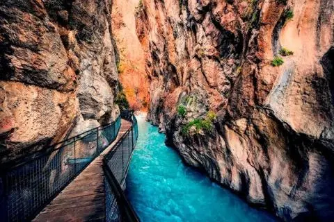 Wooden walkway beside turquoise canyon water, narrow and rocky walls