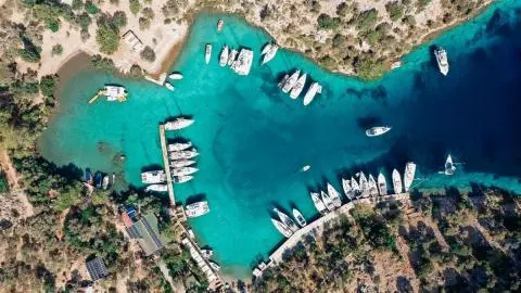 Drone view of sailboats and motor yachts moored along piers in a turquoise cove