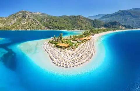 Sandy beach with rows of umbrellas and turquoise water by a yacht