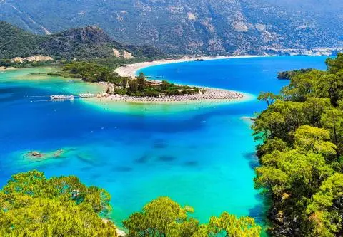 Turquoise bay with sandy spit and pine coast, calm blue water