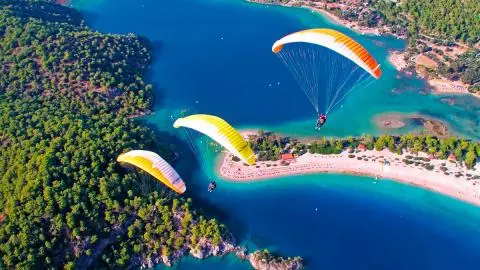 Three colorful paragliders flying over turquoise bay, beach and forested coastline