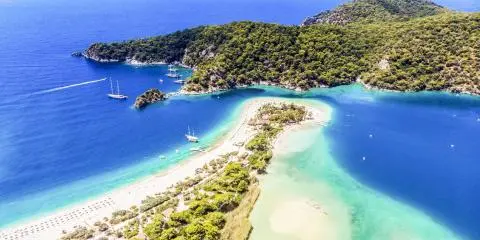 Aerial view of a narrow sandy spit, turquoise shallow water and anchored sailing yachts