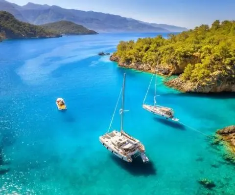 Two catamarans anchored in turquoise Cove with rocky cliffs in background