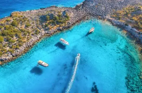 Aerial view of three anchored sailing yachts and a motorboat in a small turquoise cove