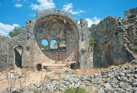 Ancient stone ruin with arched doorway and circular window, seaside backdrop