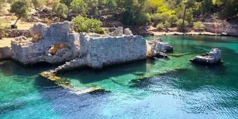 Stone quay ruins on a Turkish shore with clear turquoise water and rocky islets