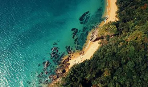 Aerial view of turquoise sea meeting rocky shoreline and sandy coves