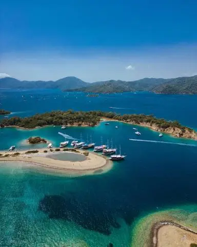 Aerial view of turquoise water around small islands with white sandy beaches and sailboats anchored