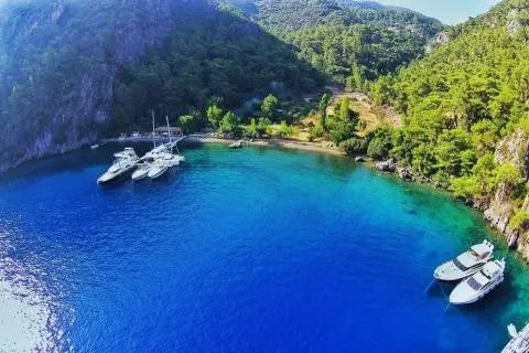 Yacht anchored along a cliffside bay with clear blue water and green hills