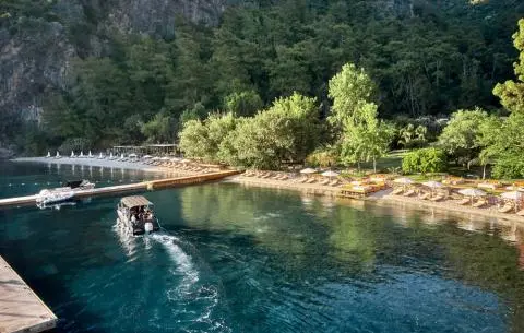 Small boat docked along a tree-lined cove with rocky shoreline and calm blue water
