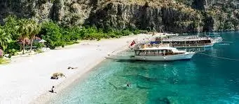 White pebble beach with turquoise water and wooden charter boats moored nearby