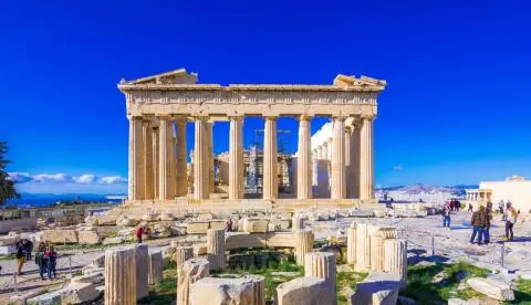 Parthenon temple facade with column ruins and visitors under vivid blue sky