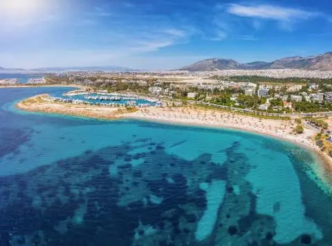 Turquoise sea with marina on a curved peninsula, sandy beach, coastal town and mountains