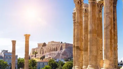 Sunlit ancient columns frame a Greek coastline and distant ruins by the sea