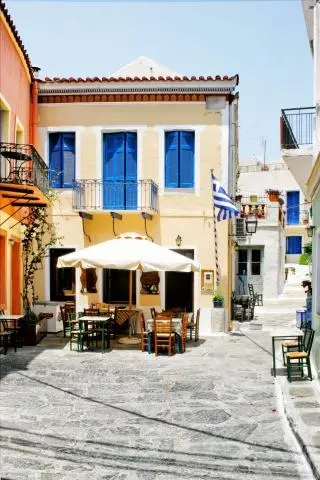 Yellow building with blue shutters and outdoor café on a narrow Greek street